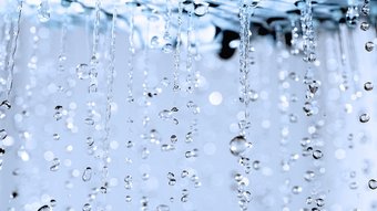 Wassertropfen, die sanft herabfallen und glitzern Eine Nahaufnahme von fallendem Wasser, das in der Luft schwebt und dabei glitzernde Reflexionen erzeugt.