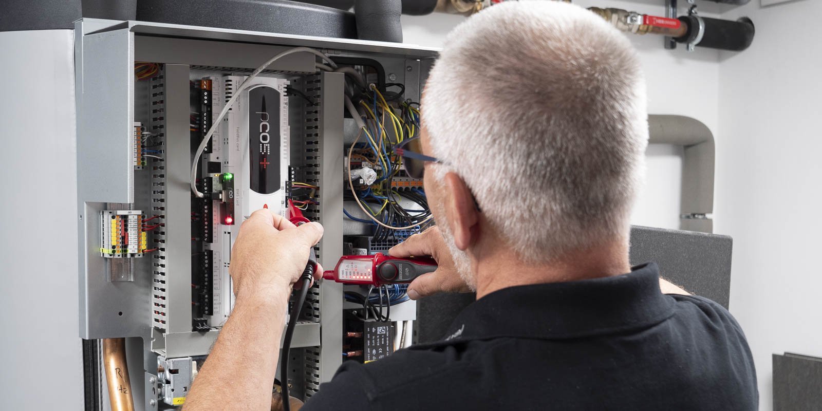Ein Techniker überprüft elektrische Verbindungen in einem Schaltschrank, während er ein Messgerät in der Hand hält.