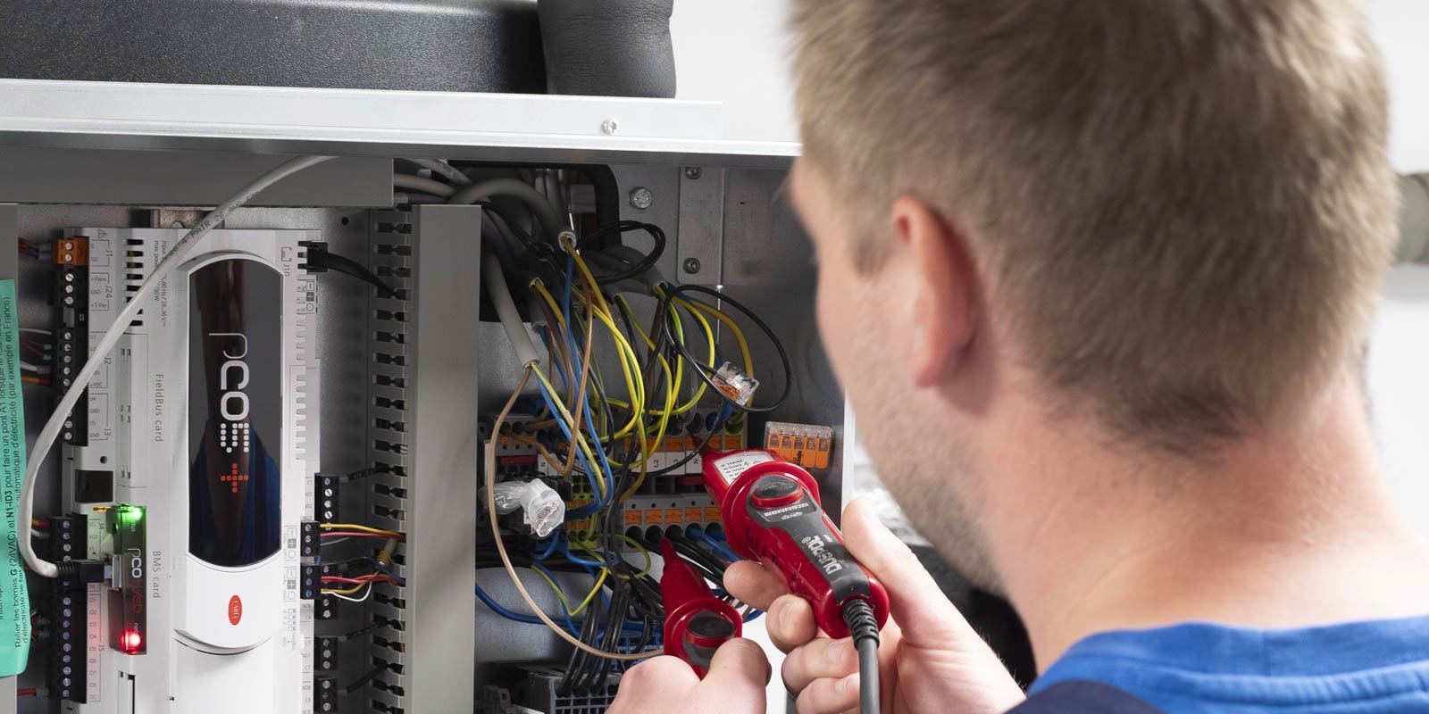 Ein Techniker überprüft elektrische Verbindungen in einem Schaltschrank, während er ein Messgerät in der Hand hält.