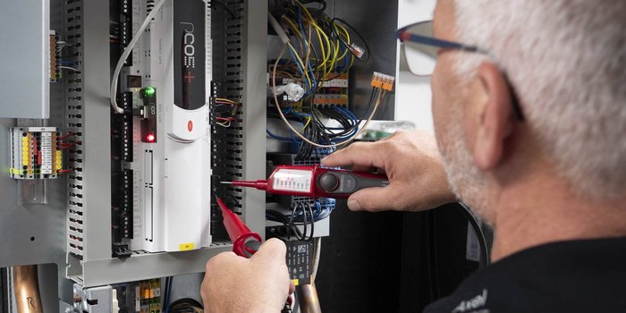 Ein Techniker überprüft mit einem Multimeter die elektrischen Verbindungen in einem Schaltschrank voller Kabel.