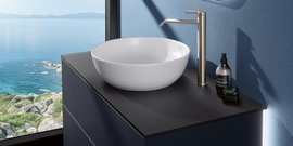 Das minimalistische Design des Waschbeckens wird durch die goldene Armatur und die sanften Farben des Raumes ergänzt.