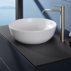 Das minimalistische Design des Waschbeckens wird durch die goldene Armatur und die sanften Farben des Raumes ergänzt.