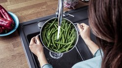 Eine Frau die die ein Topf mit Bohnen unter dem Wasser abspuehlt